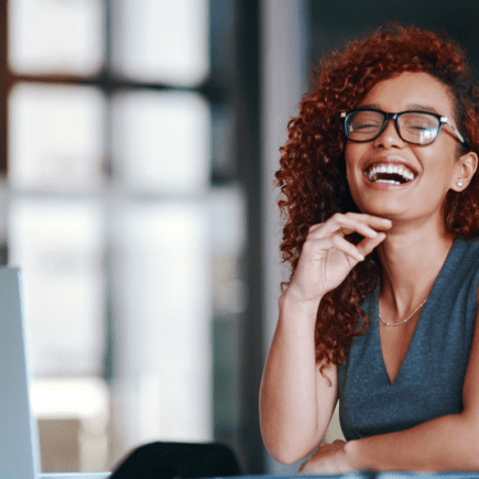 Femme souriante et productive devant son ordinateur, illustrant la clarté mentale, la sociabilité et l’énergie des phases folliculaire et ovulatoire du cycle menstruel.