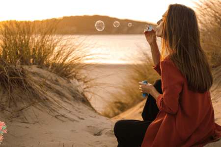 Femme assise au coucher du soleil soufflant des bulles, symbolisant les fluctuations naturelles de la libido, de l’humeur et de l’énergie selon le cycle féminin.
