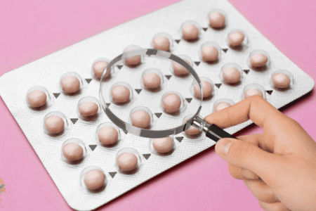 Plaquette de pilule examinée à la loupe, symbolisant l’analyse des effets secondaires et des risques hormonaux